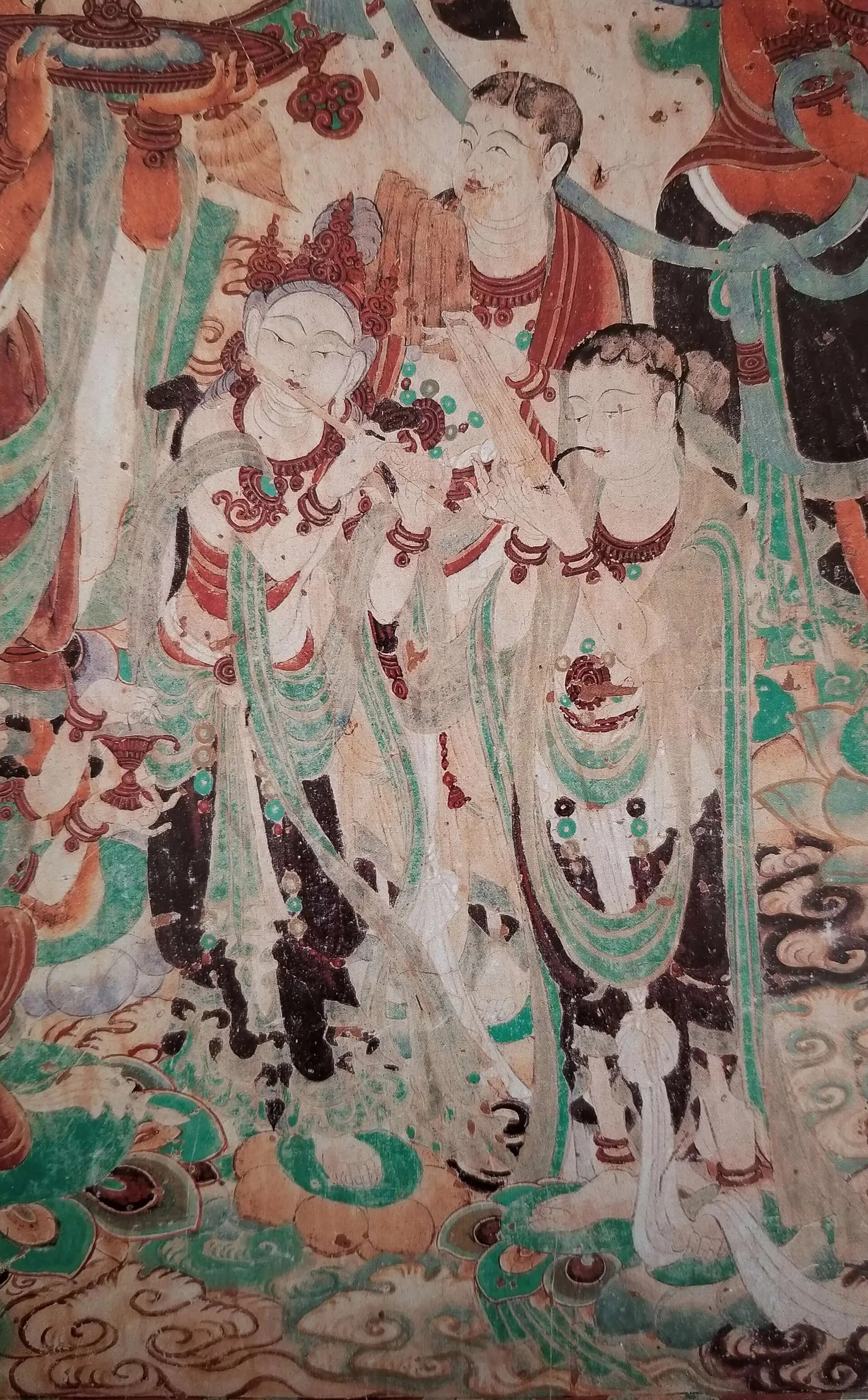 Detail of a Tang dynasty wall painting from Mogao Cave 159, showing celestial musicians in green and ochre robes, one playing a transverse flute, against a background of clouds and lotus forms.