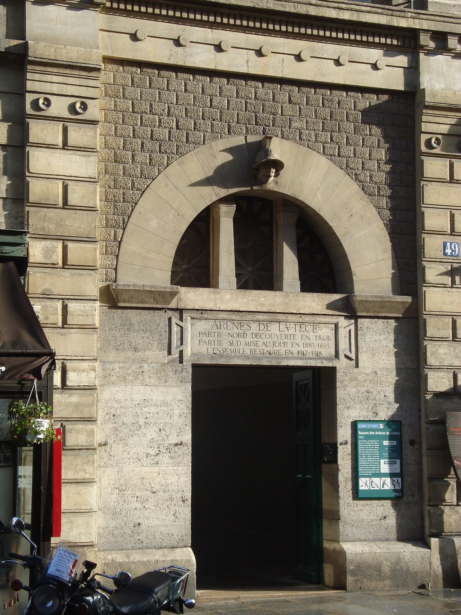 The discreet arched street entrance to the Arènes de Lutèce at 49 rue Monge, topped by a carved gladiator helmet.