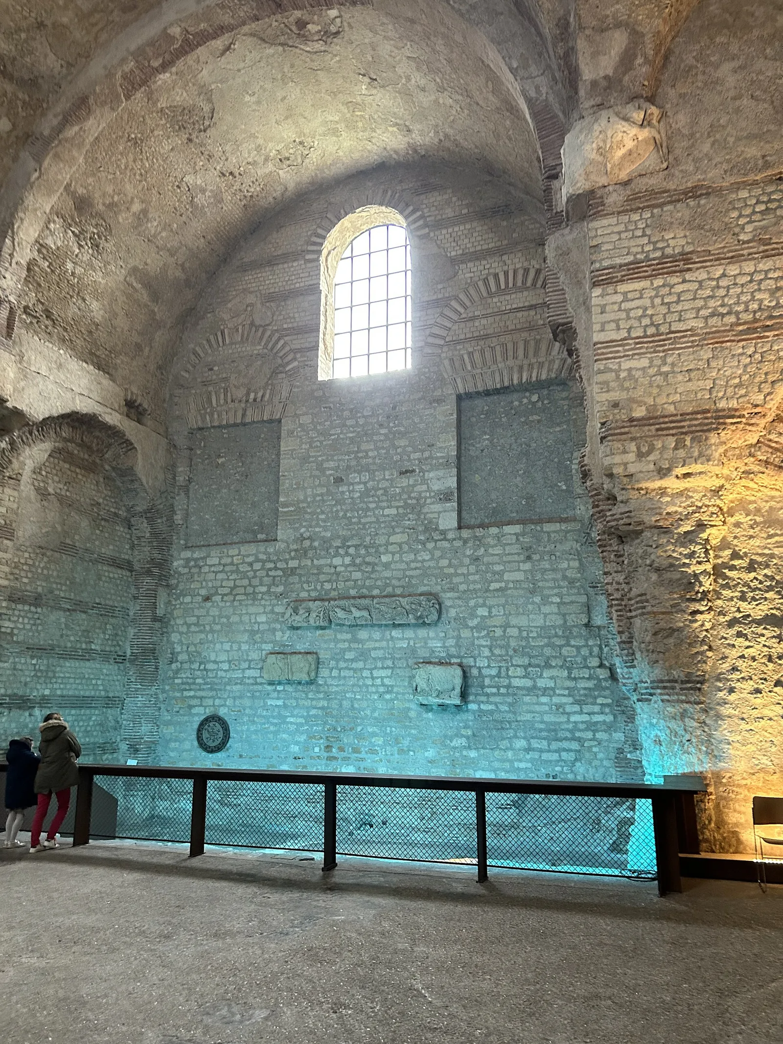 The frigidarium of the Thermes de Cluny in Paris, its Roman brick and stone walls rising to the original vault above a museum walkway.