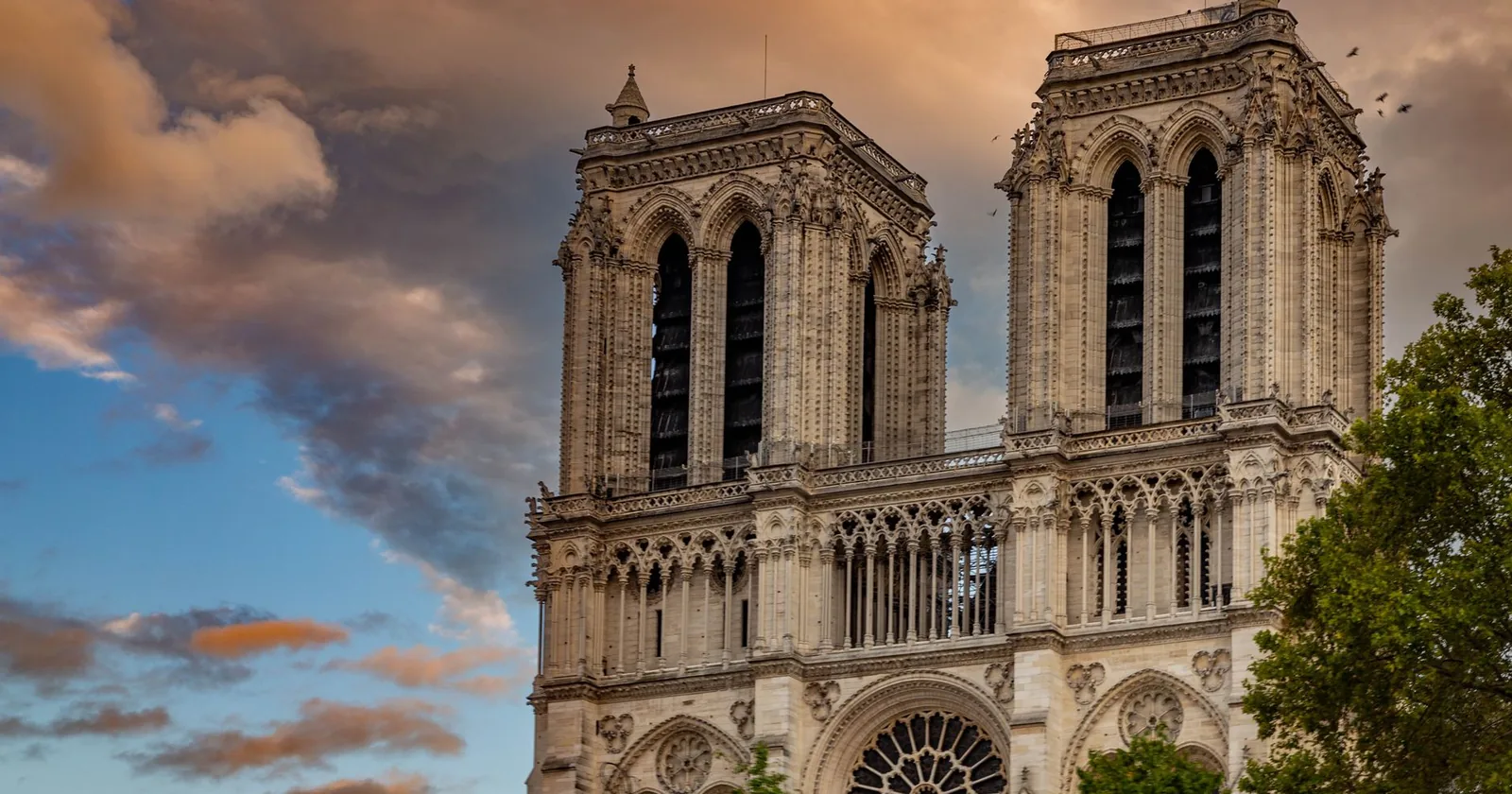 The twin square towers and rose window of Notre-Dame cathedral in Paris under a dramatic evening sky.