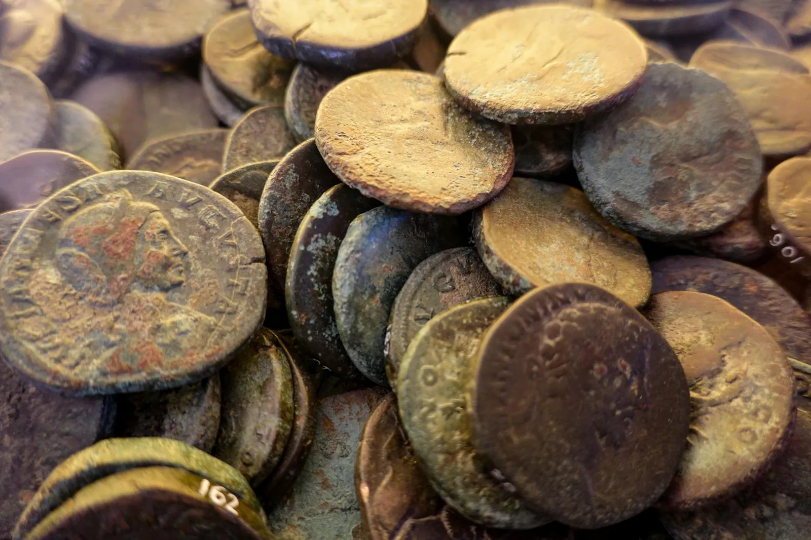A close-up pile of weathered ancient Roman bronze coins with green and brown patina.