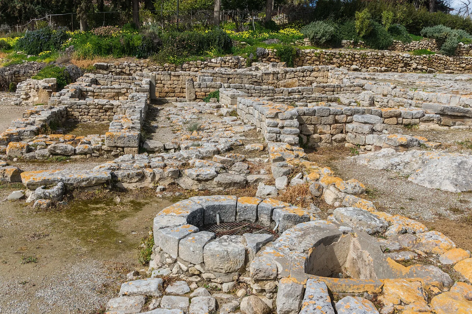 Low stone walls and a round stone-lined well among the excavated ruins of the Minoan palace at Phaistos.
