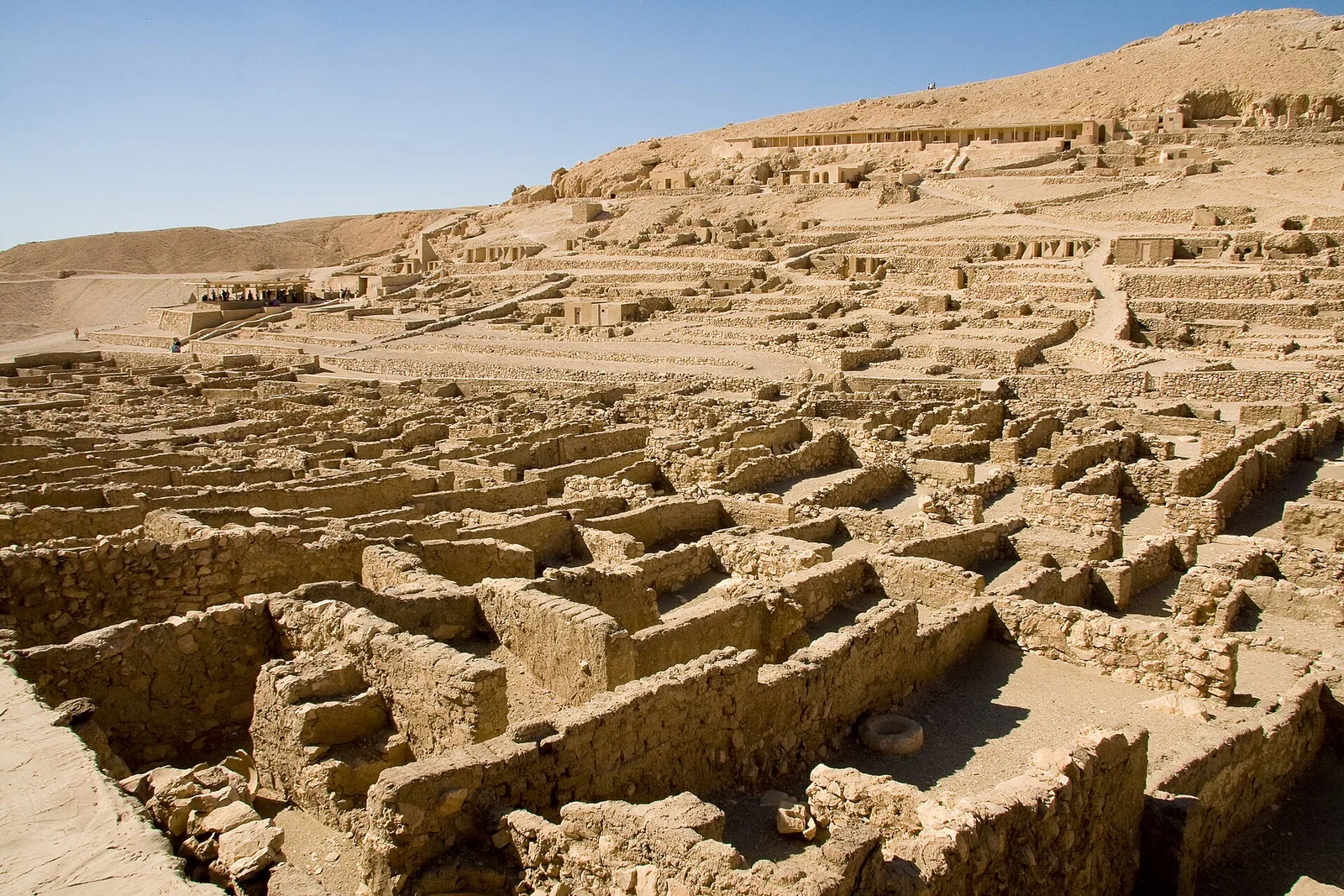 The dense grid of stone and mud-brick house foundations of the Deir el-Medina workers' village, with rock-cut tomb chapels on the hillside above.