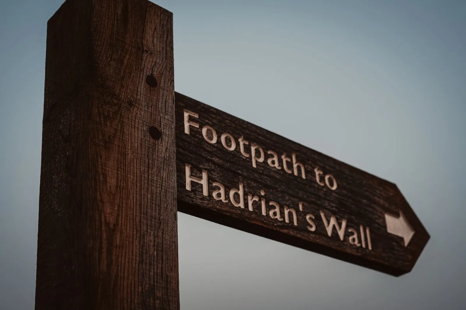 Wooden footpath signpost pointing to Hadrian's Wall