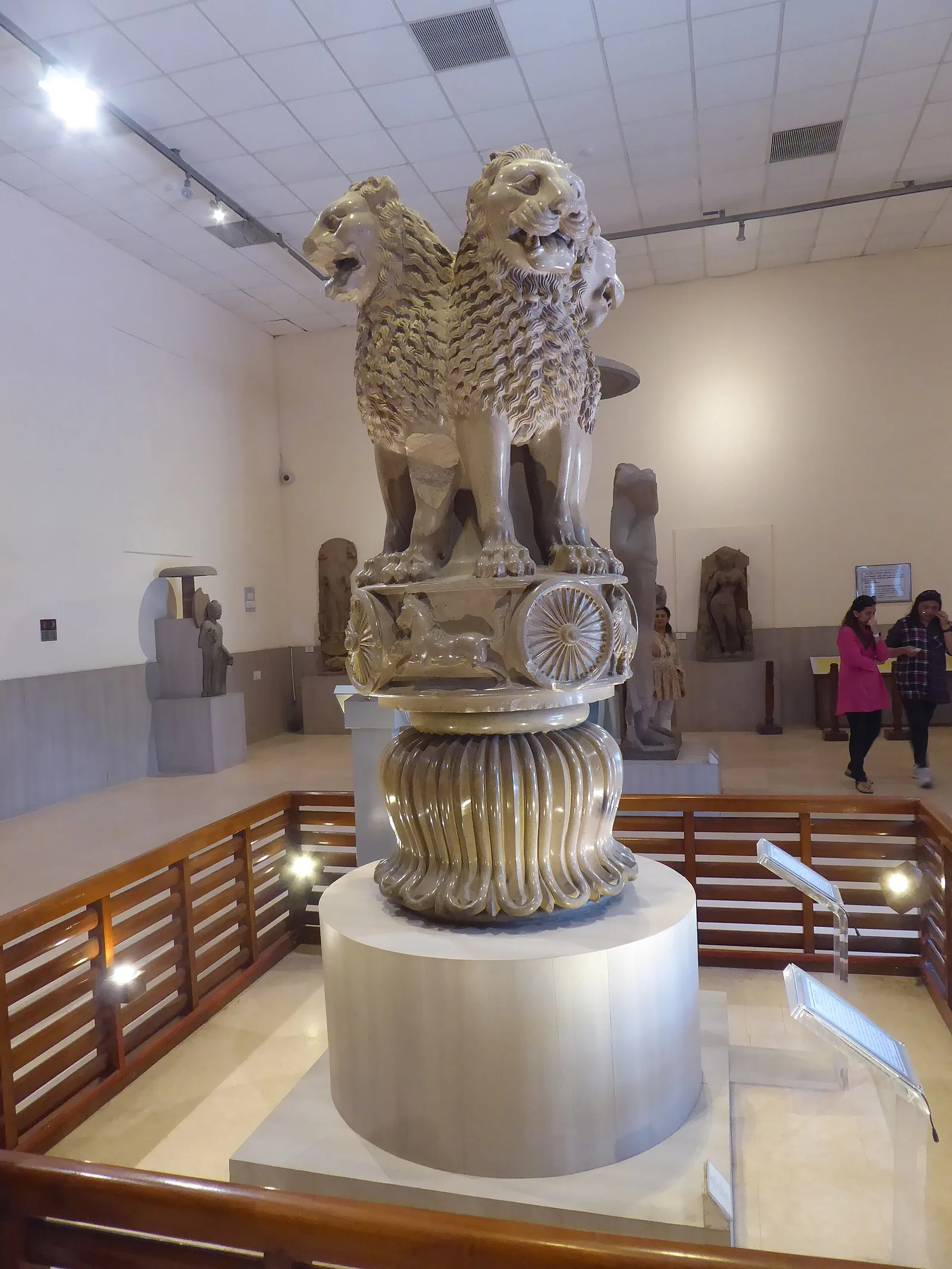 The Lion Capital of Ashoka displayed on a plinth in the Sarnath Archaeological Museum, showing four addorsed lions above a carved abacus and lotus bell.