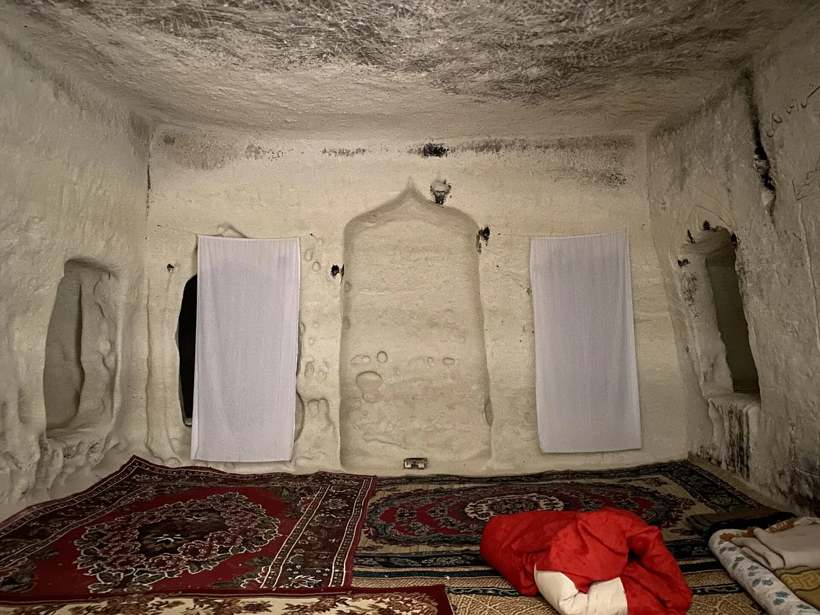 The chalk-cut prayer chamber and mihrab niche of the Shakpak-Ata mosque in Mangystau, with prayer rugs laid on the floor.