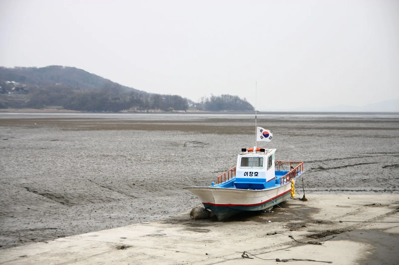 A small fishing boat resting on the mud of a Korean tidal flat at low tide, Ganghwa Island.